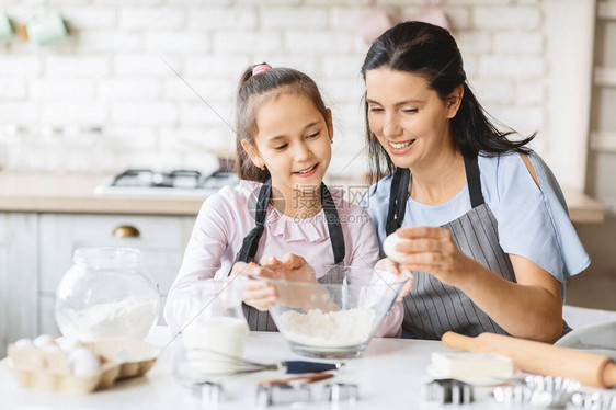 可爱的小女孩和她美丽的母亲在家一起做饭图片