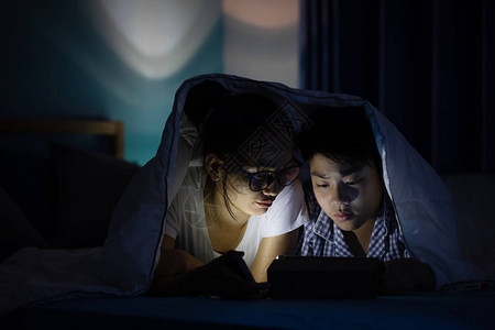 亚洲家庭的年轻母亲带着儿子在床上玩手机或智图片