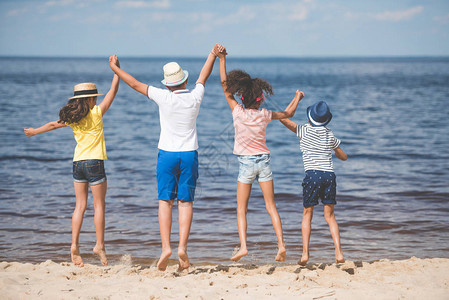 海边一起跳跃的孩子们手牵的背影图片