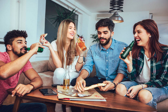 一群年轻朋友在家里吃披萨喝啤酒和看电视图片