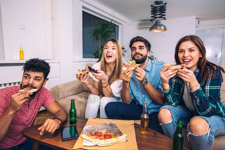 一群年轻朋友吃披萨看电视家庭派图片