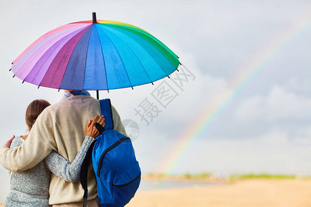 在农村环境中背着包站在多彩雨伞下的图片