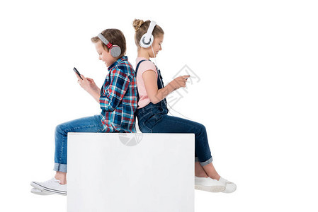 儿童在耳机中使用智能手机同时坐在立方体图片