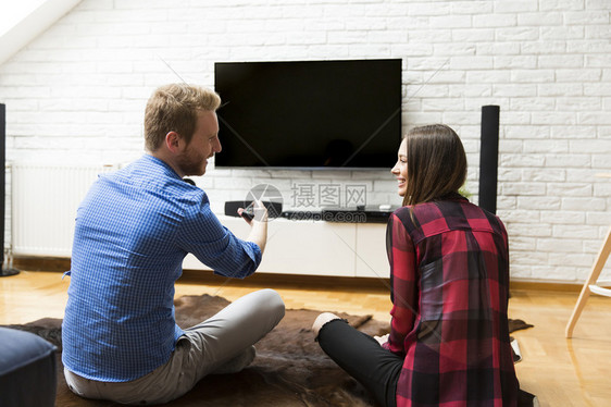 年轻夫妇在看电视坐在地板上舒适地坐着图片
