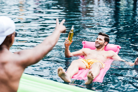 带着啤酒的微笑男子躺在游泳池的充气床垫上背景图片