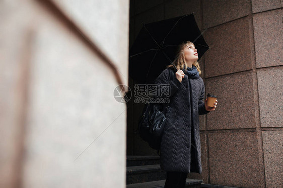 美丽的女士的肖像站在街上拿着黑色雨伞和咖啡图片