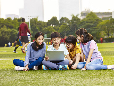 坐在操场草地上看笔记本电脑的亚裔小学儿童组别手图片
