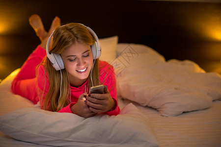 年轻漂亮的金发女人微笑着用智能手机的耳机听音乐图片