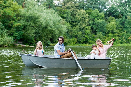 年轻微笑的家庭在公园湖边的船上图片