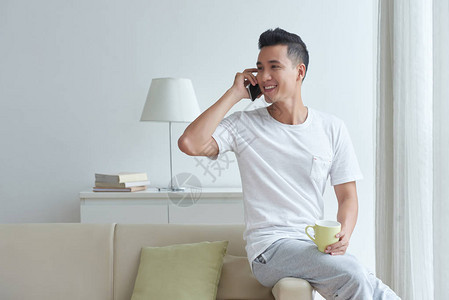 英俊的亚洲年轻男人在沙发上坐着一杯咖啡茶图片