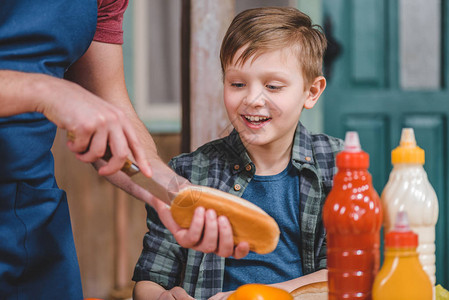 微笑的小男孩看着父亲切面包做热狗图片