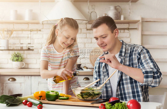 积极的爸和小女儿在家里的厨房做饭男人教女孩添加适量的沙拉图片