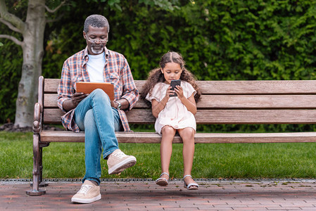 坐在公园的长凳上时使用智能手机和数字平板电脑的外祖父与可图片