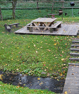 烧烤晚会的木桌和椅位于寒流附近的秋叶绿林中图片