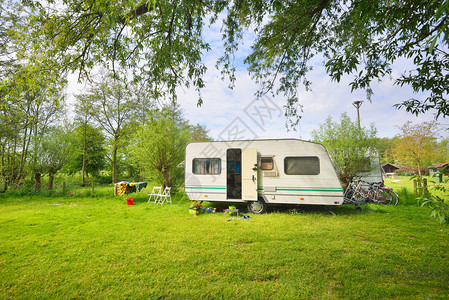 露营地绿色草坪上的白色大篷车拖晴天春天的风景欧洲生活方式旅行生态旅游公路旅行旅程假期娱乐交通背景图片