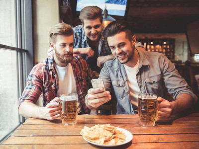 帅哥朋友在喝啤酒用智能手机在酒吧休图片