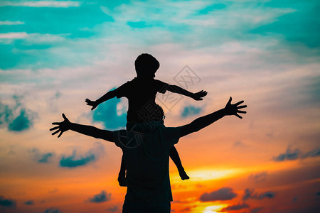 快乐的父亲和儿子在日落的天空玩游戏为图片