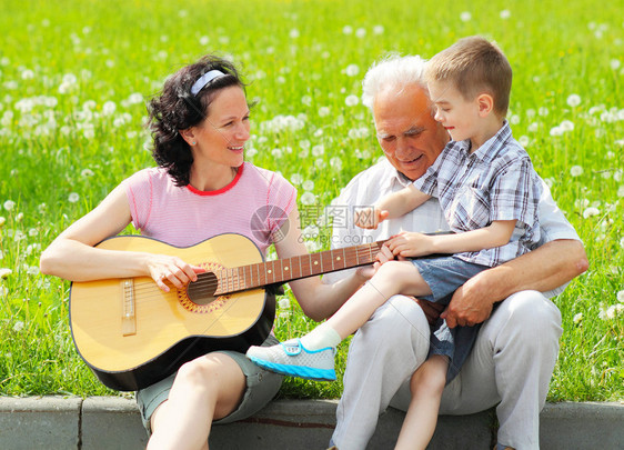 年轻快乐的母亲为她年幼的孩子和祖父弹吉他三代人与吉图片