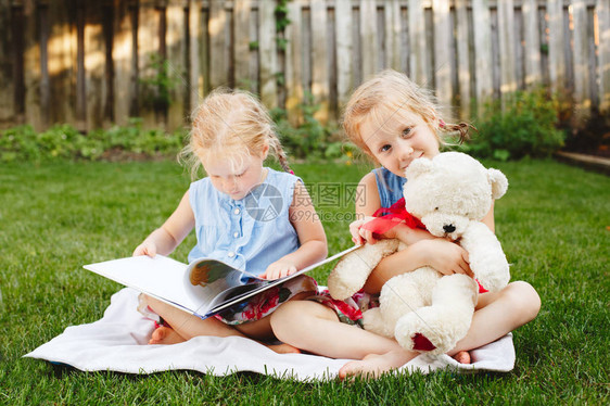 两个可爱的白人儿童朋友坐在外面的草地上拿着书的集体肖像学龄前女孩姐妹在后院看书回到图片