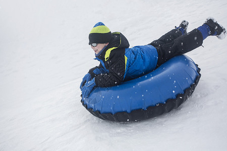 小男孩在冬日雪橇下雪山在寒冷的日子里图片