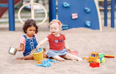 与朋友分享两个可爱的白种人和西班牙裔拉丁婴儿坐在沙箱里玩塑料彩色玩具小女孩们在操图片