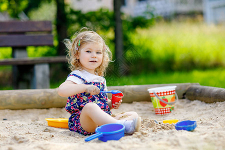 可爱的蹒跚学步的女孩在户外操场上的沙子里玩耍穿着红色裤子的漂亮宝贝在阳光明媚的温暖夏日玩乐有五颜六色的沙子玩具的孩子户外健康活跃图片