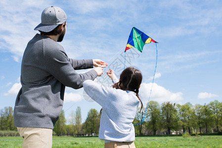 父亲和女儿在草地上放风筝的后视图图片