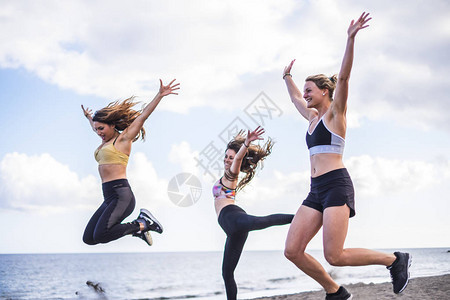 三个美丽的白人女孩在沙滩上跳跃做健身锻炼以海洋为背景的女群体户外图片