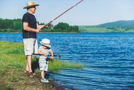 活跃的祖父和孙子在湖岸钓鱼图片