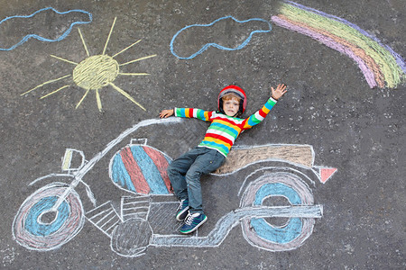 快乐的小男孩戴着头盔玩着用彩色粉笔画的摩托车画图片
