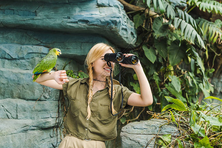 身穿狩猎西装的快乐年轻女子手抱鹦鹉在丛林中通背景图片