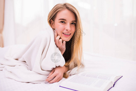 女孩在床上看书躺在肚子上笑在家闲暇的一图片