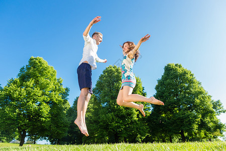 恋爱中的情侣在公园草坪上跳跃图片