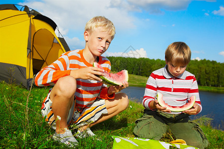 两名男孩在营地附近的绿草上吃西图片
