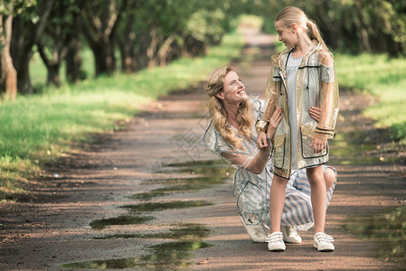 金发母亲和可爱的女儿穿着透明的雨衣在公园图片