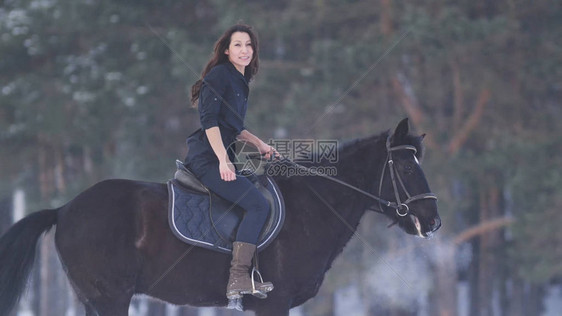 美丽的长发美女骑着黑马穿过森林的雪远光图片