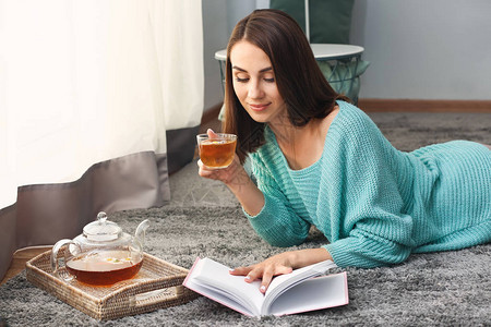 美丽的年轻女子在家读书时喝茶图片