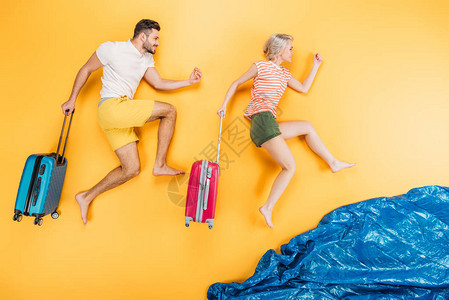 快乐的年轻赤脚夫妇带着手提箱跑在黄色图片