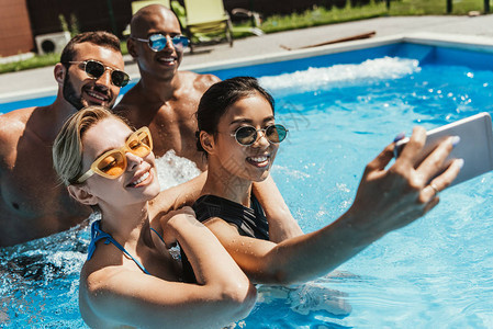 穿着太阳眼镜的多文化夫妇在游泳池里用智能图片