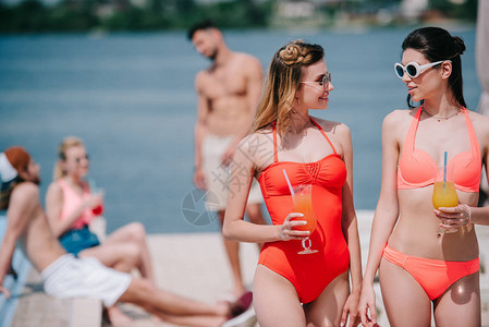 穿着泳装的漂亮女孩拿着夏季鸡尾酒在海滩上图片