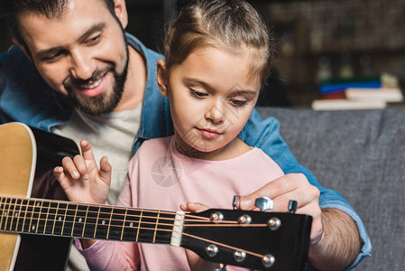 英俊的年轻父亲学习小女儿弹吉他图片