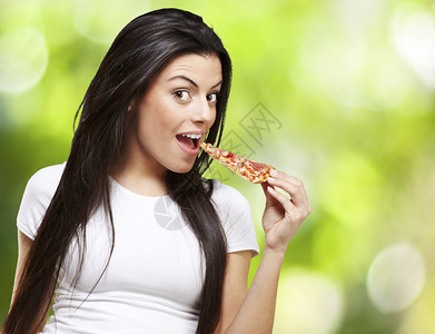 年轻女在大自然背景下吃一块比萨图片
