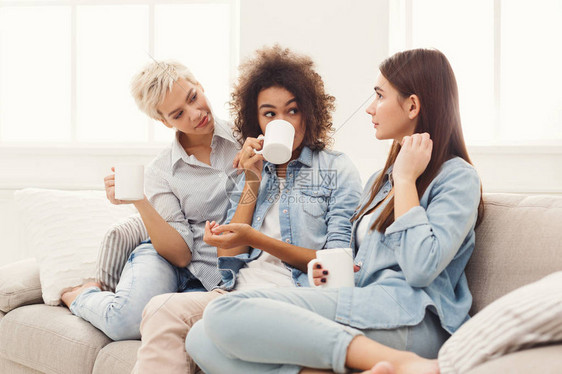 三个端着咖啡杯的年轻女人在沙发上聊天图片