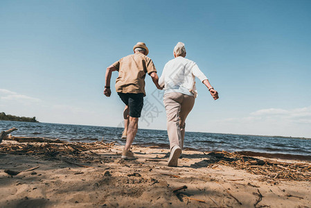 老年夫妇牵手在沙滩上奔跑的背影图片