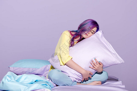 困倦的年轻女子坐在床上拥抱枕头图片