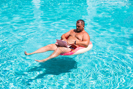 男商人在游泳池的水里戴着一个充气环图片