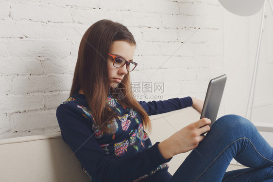 眼镜戴眼镜的女孩与小工具平板电脑坐在沙发上青春期图片