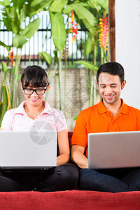 坐在沙发上用笔记本电脑坐着的印度尼西亚年轻夫妇图片