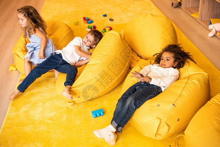 在幼儿园坐在黄色豆袋椅上的多文化儿童高角度图片