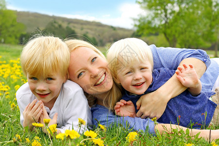 一个快乐的年轻母亲躺在外面拥抱她的两个孩子在春日的丹德利图片